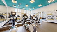 Located at 100 Dalton Ln in Charlottesville, VA, this fitness center is a thoughtfully designed, single-floor facility offering a comprehensive workout experience across multiple distinct zones. The space is immediately distinguished by its bold teal ceilings, bright recessed and panel lighting, and white walls adorned with motivational typography in yellow and gray — creating an energetic yet focused atmosphere throughout.

The main cardio area is generously sized, housing a full lineup of treadmills, ellipticals, and stationary bikes equipped with digital displays. Large windows allow ample natural light to fill the room, while ceiling fans contribute to comfort during workouts. Full-length mirrors amplify the sense of openness in this zone.

A dedicated studio room features warm hardwood-style flooring and provides space for rowing machines, spin bikes, yoga mats, and a dumbbell rack — ideal for group classes or individual low-impact training. A large wall-mounted flat-screen TV and mirrored wall enhance the studio's functionality.

A separate strength training area offers rubber flooring and a bold yellow-accented power rack system complete with pull-up bars, weight plates, kettlebells, medicine balls, battle ropes, and a full dumbbell rack. A glass garage-style door brings in additional natural light and connects the space to the outdoors. A connecting hallway ties all zones together seamlessly.
