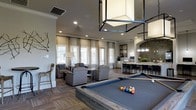 This well-appointed single-floor amenity space combines modern design with a welcoming, social atmosphere. The open-concept layout seamlessly connects a fully equipped kitchen, a comfortable lounge area, and an entertainment zone, making it ideal for gatherings and recreation.

The kitchen features sleek white cabinetry, stainless steel appliances, and a striking oversized island with a polished stone countertop, illuminated by elegant geometric pendant lights. A mosaic tile accent wall adds a bold visual element, complementing the warm, dark hardwood-style flooring that runs throughout the space.

The adjacent lounge area is furnished with plush seating arrangements, bathed in natural light streaming through large windows dressed with neutral linen drapes. Recessed lighting and crown molding along the ceiling enhance the refined character of the room.

The entertainment area centers around a full-size billiards table beneath a distinctive geometric overhead fixture, creating a focal point that adds an industrial-chic contrast to the otherwise classic interior. French doors provide access to the exterior, further brightening the space and offering a seamless indoor-outdoor connection. Together, these elements create a cohesive, upscale environment designed for both relaxation and social engagement.