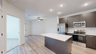 This thoughtfully designed one-bedroom, one-bathroom residence in Kansas City, MO offers a clean, modern aesthetic with high-quality finishes throughout. The open-concept layout connects the kitchen and living area, creating an efficient and welcoming flow. The kitchen is a standout feature, showcasing dark walnut-toned cabinetry that extends to the ceiling, a white quartz-topped center island, a subway tile backsplash, and a full suite of stainless steel appliances including a refrigerator with ice maker, range, microwave, and dishwasher. Light hardwood-style flooring runs through the main living areas, complementing the contemporary cabinetry and crisp white walls. The bedroom is a comfortable retreat, finished with plush carpet, large windows that invite natural light and outdoor views, and a ceiling fan for year-round comfort. A dedicated closet provides practical storage. The bathroom continues the modern design language with rich wood-toned vanity cabinetry, brushed metal hardware, a white countertop, and light tile flooring. Recessed lighting and a clean white palette throughout the unit contribute to a bright, airy ambiance. Located at 8550 N Main St, this residence combines functional design with contemporary style in a well-appointed Kansas City community.