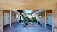 Located at 598 N Walton Ave in Yuba City, California, this multi-unit property is built around a central open-air courtyard that serves as the heart of the complex. The building's warm stucco exterior is finished in a distinctive golden-yellow tone, lending the property a welcoming and cohesive appearance. The courtyard is generously landscaped with mature trees, agave plants, and a variety of potted and ground-level plantings, creating a lush, shaded outdoor environment bathed in natural California sunlight.

The property features covered ground-floor walkways supported by structural posts, providing sheltered access to individual unit entrances. White entry doors line both the ground level and the upper floor, each accessible via a central staircase. The upper level is lined with decorative lattice-style balcony railings in a deep blue-black finish, adding an architectural accent that contrasts with the warm exterior tones. A no-smoking policy is posted throughout the shared courtyard areas.

The elongated layout of the building, as seen in the 3D model, reveals a well-organized structure with units accessible from the interior courtyard on both levels. The combination of mature landscaping, covered walkways, and open communal space makes this property a distinctive multi-unit offering in the Yuba City area.
