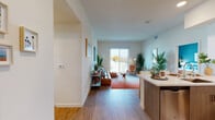 This single-floor residence features a thoughtfully designed open-concept layout that connects the kitchen, dining, and living areas seamlessly. The kitchen is equipped with stainless steel appliances, including a refrigerator, electric range, and over-the-range microwave, complemented by two-tone cabinetry in white and warm wood tones, a subway tile backsplash, and light hardwood flooring. A peninsula with quartz-style countertops provides additional prep and casual dining space.

The living area is anchored by a large sliding glass door that fills the room with natural light and offers views of the surrounding neighborhood. Hardwood-style flooring continues throughout the main living spaces, contributing to a warm, cohesive aesthetic.

The bedroom is carpeted and features a large picture window with outdoor views, providing a bright and restful environment. The full bathroom includes a wood-toned vanity with a white undermount sink, a large mirror, and a shower-tub combination.

A stacked washer and dryer unit is conveniently housed within the residence. Overall, the space maintains a clean, contemporary design with neutral tones and modern fixtures throughout.