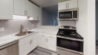 Located at 50 Holy Family Rd in Holyoke, Massachusetts, this thoughtfully renovated single-floor unit showcases a clean, modern aesthetic throughout. The kitchen is outfitted with white shaker cabinetry, marble-style countertops, a classic subway tile backsplash, and stainless steel appliances including an electric range and over-the-range microwave. A pass-through opening connects the kitchen to the living area, enhancing the sense of openness between the two spaces. The living area features durable gray wood-tone flooring and neutral gray walls, creating a contemporary and cohesive feel. Large windows allow natural light to fill the room while offering views of the surrounding neighborhood. The bedroom continues the bright, neutral palette with plush carpeting and its own large window framing outdoor views. The bathroom is finished with elegant marble-style tile covering the floors, vanity countertop, and full tub/shower surround. Brushed gold hardware accents the space, complementing the white cabinetry and providing a refined touch. The overall layout, visible in the 3D overview, is well-organized and functional, with a central hallway connecting the key living spaces. This unit combines practical updates with stylish finishes throughout.