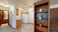 Located at 9215 Nicollet Ave S in Bloomington, Minnesota, this single-floor residence offers a practical and comfortable layout across two bedrooms, one bathroom, a kitchen, and a hallway. The kitchen is equipped with warm honey-toned wood cabinetry, a white refrigerator, and an electric range with overhead ventilation. Light wood-style flooring runs through the kitchen area, while a built-in wood bookshelf adds functional character near the entryway. A ceiling fan with a light fixture provides overhead circulation and illumination in the kitchen space. The bedrooms feature plush gray carpeting and neutral walls, creating a calm and restful atmosphere. The primary bedroom is generously sized, highlighted by a large picture window with vertical blinds that allows natural light and outdoor views, complemented by a ceiling fan overhead. An expansive wall of louvered bi-fold closet doors provides substantial storage. The second bedroom also features carpeting and multiple electrical outlets along the baseboard. The bathroom offers a full vanity with wood cabinetry, a white countertop sink, mosaic tile flooring, and a tiled tub/shower combination. Baseboard heating is present throughout, ensuring efficient warmth. Overall, the residence presents a clean, functional design well-suited for comfortable everyday living.
