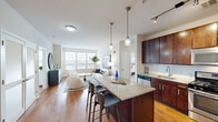 This well-appointed 2-bedroom, 2-bathroom residence at 303 Main St. in Hempstead, NY offers a thoughtfully designed single-floor layout. The open-concept kitchen is a standout feature, showcasing rich dark-wood cabinetry, stainless steel appliances, a subway tile backsplash, and a granite-topped island with bar seating, all illuminated by stylish pendant lighting. The kitchen flows seamlessly into the dining area and living room, where warm hardwood flooring and large windows invite an abundance of natural light. The living room offers a welcoming, modern atmosphere with generous windows overlooking the outdoors. A dedicated dining nook provides an intimate setting for meals. Both bedrooms are carpeted and tranquil, with the primary bedroom featuring a wide window bank with outdoor views and ample space. The second bedroom is equally comfortable, with soft neutral tones and well-placed lighting. Two full bathrooms are finished with dark wood vanities, white countertops, and tiled tub-shower combinations. Two closets provide practical storage throughout the residence. The overall aesthetic is clean and contemporary, with a neutral palette, quality finishes, and a cohesive design that balances comfort and style.