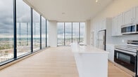 Located in the heart of Cincinnati at 29 Seventh St W, this contemporary two-bedroom, two-bathroom residence offers a refined urban living experience with striking architectural details. The open-concept kitchen and living area is the centerpiece of the home, anchored by dramatic floor-to-ceiling windows that frame sweeping panoramic views of the Cincinnati skyline and beyond. Light wood flooring runs throughout, complementing the bright, neutral palette that defines the space.

The kitchen is well-appointed with soft gray shaker-style cabinetry, stainless steel appliances including a refrigerator, range, and built-in microwave, a herringbone tile backsplash, and an expansive white quartz waterfall island with an undermount sink — ideal for both cooking and casual dining.

The generously sized primary bedroom enjoys its own floor-to-ceiling window with city views, while both bedrooms are served by dedicated closets. A bright hallway connects the private quarters to the main living areas. The two bathrooms are finished with large-format white tile; one features a soaking tub-shower combination, while the other offers a glass-enclosed walk-in shower. Clean lines, recessed lighting, and an abundance of natural light give the entire residence a polished, modern ambiance.
