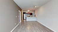This well-designed single-floor unit offers a thoughtful layout that balances open living spaces with functional private areas. The entry opens into a spacious living area finished with light-toned wood-look flooring and neutral painted walls, creating a bright and welcoming atmosphere. Track lighting accents the ceiling, adding both style and practicality to the main living space.

The kitchen is a standout feature, showcasing rich dark-stained cabinetry, granite-style countertops, and a full suite of stainless steel appliances including a refrigerator, range, and microwave. A peninsula with seating overhang provides a natural gathering point and separates the kitchen from the living area. Eye-catching red pendant lights hang above, adding a bold design touch. A stacked washer and dryer unit is conveniently tucked nearby within the living space.

The bedroom is carpeted for comfort and includes a generously sized walk-in closet equipped with wire shelving and hanging rods. The full bathroom features a dark-stained vanity with a light countertop, a large mirror, and a tub-shower combination enclosed with sliding glass doors, all set on wood-look tile flooring.

Completing the unit is an attached two-car garage with a concrete floor and automatic opener, offering direct interior access — a practical and valued amenity.