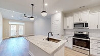 Located at 9000 Palm Passage Loop in Summerville, SC, this well-appointed single-story home offers three bedrooms and two bathrooms thoughtfully arranged across a comfortable floor plan. The open-concept kitchen and living area serves as the heart of the home, showcasing white shaker cabinetry with sleek matte black hardware, a classic subway tile backsplash, and stainless steel appliances including a range, microwave, and refrigerator. A large center island with a striking granite countertop and an undermount sink with a matte black faucet provides both workspace and casual seating, illuminated overhead by contemporary globe pendant lights. Light hardwood-style flooring flows throughout the main living areas, complementing the home's clean, neutral color palette. The spacious primary bedroom features vaulted ceilings, a ceiling fan, and French doors that open to an outdoor balcony, flooding the room with natural light. Additional bedrooms are finished with plush carpet and natural light from well-placed windows. Both bathrooms are elegantly appointed with granite vanity tops, white shaker cabinetry, matte black fixtures, and large mirrors. The cohesive design aesthetic—modern finishes paired with a bright, airy feel—gives this home a fresh and welcoming ambiance throughout.