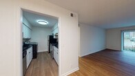 This single-floor residence offers a clean, modern aesthetic carried consistently throughout its well-organized layout. The living area is bright and open, featuring warm wood-look flooring and a sliding glass door fitted with vertical blinds that provides direct access to an outdoor space while allowing natural light to fill the room. The open sightlines from the living area connect seamlessly to adjacent spaces, creating a cohesive flow.

The galley-style kitchen is thoughtfully appointed with white shaker cabinetry, dark granite-style countertops, and a subway tile backsplash. It includes a stainless electric range, a black refrigerator, an overhead range hood, and a built-in washer and dryer unit, making laundry highly convenient. Overhead flush lighting keeps the kitchen well-illuminated.

The bedrooms feature the same wood-look flooring, white walls, and ample natural light from windows. At least one bedroom includes a closet with bifold doors and a hanging rod for organized storage.

The bathroom is finished with large-format marble-look tile flooring, a white subway tile tub surround, chrome fixtures, and a dark-topped vanity, presenting a clean and contemporary feel throughout.