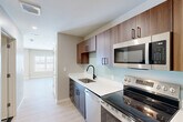 Located at 19 Hemans St in Worcester, MA, this thoughtfully designed single-floor residence offers a well-organized layout encompassing a living room, a combined dining and kitchen area, a full bathroom, in-unit laundry, a utility room, two closets, and a dedicated entrance. Light-toned hardwood-style flooring runs throughout, complementing the neutral warm-beige walls and recessed lighting that give the space a clean, contemporary feel. The open-concept kitchen is outfitted with rich walnut-toned upper and lower cabinetry, white quartz countertops, a matte black faucet, and a full suite of stainless steel appliances including a refrigerator, electric range, microwave, and dishwasher. A soft aqua backsplash adds a subtle pop of color. The living room is bright and airy, featuring large windows and a sliding glass door that opens to a private balcony with sweeping views of the surrounding Worcester hillside. The bathroom is finished with large-format gray tile flooring, dark cabinetry, and a tiled walk-in shower enclosed with a curved black rod. The living area also includes a closeted storage space, rounding out this efficiently designed, modern residence.