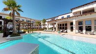 This single-story residence is part of a well-appointed community characterized by Mediterranean-inspired architecture, featuring a striking white stucco exterior with terracotta-accented rooflines and pergola-shaded courtyards. The centerpiece of the community amenities is a generously sized resort-style pool surrounded by lounge seating, lush landscaping, and an expansive covered patio—ideal for outdoor relaxation.

Inside, the open-concept floor plan seamlessly connects the living, dining, and kitchen areas into a cohesive, flowing space. Rich hardwood flooring runs throughout, lending warmth and continuity to the interior. The living area is well-lit by multiple windows dressed in classic plantation shutters and linen drapes, with a ceiling fan adding both style and comfort overhead.

The kitchen is finished with dark espresso cabinetry, granite countertops, stainless steel appliances, and a breakfast bar with pendant lighting—making it both functional and visually striking. Adjacent to the kitchen, the dining area features a chandelier overhead, providing an inviting setting for entertaining.

The entryway is accented with decorative wall art and a console table, creating a welcoming first impression. Throughout the residence, neutral tones and thoughtful design details contribute to a comfortable and cohesive aesthetic.