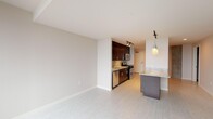 This single-floor apartment at 150 Forest Ave in Oak Park, IL offers a thoughtfully designed living space with a modern aesthetic. The galley-style kitchen is equipped with stainless steel appliances, including a gas range, microwave, and dishwasher, complemented by dark cabinetry, granite countertops, a mosaic tile backsplash, and track lighting. A granite-topped island provides additional prep space. The open living area features light tile flooring and floor-to-ceiling windows that invite abundant natural light and outdoor views. The bedroom includes plush carpeting and a spacious closet, while the bathroom offers a granite vanity and clean tile flooring throughout.