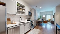 This single-floor residence offers a thoughtfully designed open-concept layout that seamlessly connects the kitchen, dining, and living areas. The kitchen is a standout feature, outfitted with crisp white shaker-style cabinetry accented by matte black hardware, a herringbone tile backsplash, granite-look countertops, and a full suite of stainless steel appliances including a side-by-side refrigerator, range, dishwasher, and microwave. Open shelving adds both function and visual interest to the space. Polished concrete flooring runs throughout the main living area, lending an industrial-modern character to the home. The living room is bright and welcoming, anchored by a private entry door with sidelights that usher in natural light. Elevated ceilings throughout enhance the sense of openness and airiness. A dining area connects the kitchen and living space, making the floor plan ideal for both everyday living and entertaining. The bedroom is a serene retreat with carpeted flooring, high ceilings, and a calm, neutral palette. It is complemented by a generously sized walk-in closet fitted with wire shelving and hanging rods, offering ample storage. The overall design strikes a balance between modern finishes and comfortable livability.