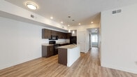 Located at 355 N Mill Rd in Vineyard, Utah, this single-floor residence offers a clean, modern design with a thoughtful layout throughout. The open-concept kitchen and living area serves as the heart of the home, showcasing rich dark wood cabinetry, light granite countertops, and a central kitchen island with a built-in sink — ideal for both meal preparation and casual dining. Black appliances, including a range, microwave, and refrigerator, complement the contemporary aesthetic, while pendant lighting and recessed fixtures provide layered illumination. Light wood-style flooring runs throughout the main living and kitchen areas, adding warmth and continuity to the space. A hallway leads to the private sleeping quarters, where plush carpeting creates a comfortable underfoot feel. The bedrooms are generously sized, filled with natural light from large windows fitted with blinds, and include walk-in closets offering ample storage. The bathrooms maintain the same cohesive design language, featuring wood-look flooring, dark vanity cabinetry with granite countertops, brushed nickel hardware, and full tub-shower combinations. The overall ambiance throughout the residence is bright, neutral, and move-in ready, reflecting a modern and functional living environment.