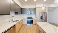 This well-appointed single-floor residence showcases a thoughtfully designed layout with contemporary finishes throughout. The kitchen serves as a standout centerpiece, featuring a two-tone cabinet design that combines warm natural wood lower cabinets with charcoal upper cabinetry, all complemented by crisp white quartz countertops and a striking hexagonal tile backsplash. A central island with pendant lighting adds both functionality and style, while stainless steel appliances — including a refrigerator, range, microwave, and dishwasher — complete the modern aesthetic. Light wood-style flooring flows through the main living areas, adding warmth and continuity.

The bedrooms are finished with plush carpeting and ceiling fans, and each includes generous closet space with built-in shelving and hanging rods — one room features a dual-door walk-in closet configuration. Natural light filters in through well-placed windows with views of the surrounding community.

The bathrooms are elegantly appointed with marble-look tile flooring and surround, wood-toned vanity cabinetry, white quartz countertops, and large framed mirrors with bright vanity lighting. A sliding glass-enclosed soaking tub adds a refined touch.

Practical convenience is provided by an in-unit stacked washer and dryer tucked neatly into a dedicated closet, rounding out this polished and functional residence.