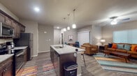 Located at 750 S Promenade Blvd in Rogers, Arkansas, this well-appointed single-floor unit offers a thoughtfully designed open-concept layout that seamlessly connects the kitchen, dining, and living areas. The kitchen is a standout feature, showcasing rich dark-stained cabinetry extending to the ceiling, granite-look countertops, stainless steel appliances including a refrigerator, electric range, and microwave, and a central island with an undermount sink and pendant lighting above — ideal for both meal prep and casual dining. Wood-look plank flooring runs throughout, adding warmth and continuity across the space. The living area is generously sized, featuring a ceiling fan, large windows that invite natural light, and room for comfortable seating arrangements. A dedicated dining space sits adjacent to the kitchen, completing the open-plan flow. Both bedrooms are well-proportioned, each equipped with a ceiling fan, ample natural light from sizable windows, and closet access. The bathroom includes dark wood vanity cabinetry, a tub/shower combination, and coordinating finishes. A dedicated in-unit laundry room with wire shelving provides added practicality. The overall aesthetic is modern and cohesive, with neutral tones and contemporary fixtures throughout.