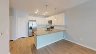 This single-floor residence offers a clean, modern aesthetic with a thoughtfully designed layout. The open-concept kitchen serves as the heart of the home, showcasing white shaker-style cabinetry, a subway tile backsplash, quartz countertops, and a full suite of stainless steel appliances including a French door refrigerator, electric range, and built-in microwave. A central island with a sink and pendant lighting above provides both additional workspace and a natural gathering point, seamlessly connecting to the main living area, which features warm wood-look flooring throughout.

The bedroom features plush wall-to-wall carpeting and two generously sized windows fitted with blinds, allowing natural light to fill the room while a ceiling fan ensures year-round comfort. An adjacent walk-in closet offers practical storage with multiple tiers of wire shelving and hanging rods, maximizing organizational capacity.

The bathroom is finished with a wide, white vanity topped with a taupe quartz countertop, an undermount sink, and a large framed mirror illuminated by an overhead light bar. Light wood-look flooring and neutral gray walls lend the space a calm, contemporary feel. Overall, the residence presents a cohesive, move-in-ready environment with consistent modern finishes and a functional, well-connected floor plan.