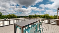 Located at 111 N Marietta Pkwy NE in Marietta, Georgia, this rooftop deck offers a compelling open-air retreat with sweeping panoramic views of the surrounding treetops and cityscape. The spacious deck is finished with light gray wood-tone composite decking and enclosed by a painted railing system that frames the views on all sides.

The space is furnished with multiple distinct seating areas designed to accommodate a variety of uses. A high-top bar table with vibrant teal bar stools serves as a social focal point, complemented by a separate lounge area featuring low-profile chairs arranged around a round accent table — ideal for casual conversation or relaxation. The juxtaposition of the teal furnishings against the neutral deck and railing creates a visually inviting atmosphere.

A defining architectural feature of the rooftop is the exposed red brick wall of the building's rooftop structure, which adds a warm, industrial character to the space. A single door provides access to and from the rooftop level. The open sky above allows for abundant natural light throughout the day, with the lush green canopy of Marietta's trees providing a verdant backdrop. The overall ambiance is relaxed yet elevated, making this rooftop deck a functional and attractive outdoor amenity.