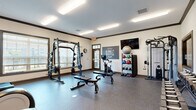 Located in Smyrna, Tennessee, this fitness center delivers a comprehensive workout facility within a single, efficiently organized space. The room features durable speckled rubber flooring throughout, providing a safe and resilient surface suited for a wide range of exercise activities. Crown molding with dark trim accents the upper walls, adding a polished architectural touch to the utilitarian space.

The facility is thoughtfully divided into distinct workout zones. A cardio section houses multiple treadmills and elliptical trainers, each positioned in front of wall-mounted flat-screen televisions, allowing members to stay entertained during their sessions. A large mirror spans the wall in this area, enhancing the sense of openness. Adjacent to this is a strength training zone featuring a full power rack with weight plates and adjustable benches, a cable machine, and a dedicated dumbbell rack with a full range of free weights.

A separate area provides space for functional training, equipped with a stationary bike, medicine balls, kettlebells, and a stability ball neatly organized on a multi-tier rack. A motivational "Stay Humble, Hustle Hard" wall graphic adds an energetic atmosphere. Natural light filters in through multiple windows fitted with horizontal blinds, while flush fluorescent ceiling fixtures ensure consistent illumination throughout. A glass-paneled entry door completes the clean, welcoming design.