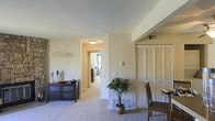 This single-floor residence at Silver Reef Student Homes offers a thoughtfully designed layout that balances comfort and functionality. The main living area features plush wall-to-wall carpeting underfoot and a textured ceiling overhead, creating a cozy and welcoming ambiance. Warm, neutral-toned walls throughout lend the space a clean and airy feel.

A defining feature of the living area is the full-width louvered closet, providing generous built-in storage. A hallway connects the living space to additional rooms, with a glimpse of a bedroom visible at the end, suggesting a well-organized floor plan. Flush-mounted ceiling lighting and wall-mounted accent lights ensure consistent illumination throughout.

Ventilation is supported by floor-level registers, keeping the space comfortable year-round. A dedicated dining area is partially visible, hinting at a layout designed to accommodate both relaxation and everyday living. Decorative touches such as a dark wood sideboard with glass cabinet doors and a potted indoor palm add warmth and character to the interior.

Overall, this residence presents a practical and comfortable living environment, well-suited for student life, with a cohesive design that emphasizes ease of living within a connected, single-level floor plan.