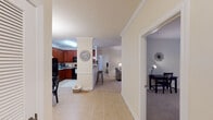 This single-floor residence offers a thoughtfully designed layout that balances open living areas with defined private spaces. The kitchen is a standout feature, equipped with rich cherry wood cabinetry, granite countertops, black appliances including an electric range and built-in microwave, and tile flooring. A peninsula with bar seating connects the kitchen to the adjoining living and dining areas, creating an open, functional flow.

The living room features crown molding and neutral-toned carpet, providing a comfortable and cohesive aesthetic. A separate den or office space off the main corridor offers added flexibility for work or leisure. The dining area is highlighted by a chandelier overhead and conveniently positioned adjacent to an in-unit laundry closet enclosed by louvered bifold doors.

Both bedrooms are carpeted and feature large windows that allow natural light to fill the rooms. Each bathroom is finished with tile flooring, cherry wood vanities, granite countertops, and a tub-shower combination. Neutral warm tones, crown molding details, and consistent finishes throughout the space lend a cohesive and welcoming ambiance across every room.