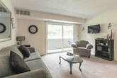 This single-floor community facility is thoughtfully designed to provide residents with a variety of functional and comfortable spaces for relaxation, entertainment, and wellness. The main lounge greets visitors with a warm and inviting atmosphere, featuring vaulted ceilings, plush seating including a sofa and accent chairs, a wall-mounted television, and a fireplace. Large windows allow natural light to fill the room, enhancing its open and airy feel, while carpeted flooring adds comfort underfoot.

Adjacent to the lounge is a dedicated media room, finished with deep green accent walls and vaulted ceilings fitted with a ceiling fan. Rows of leather recliner seating face a large wall-mounted flat-screen television, creating an immersive viewing experience. A decorative American flag artwork adds character to the space.

The fitness area is equipped with a multi-function strength training machine, free weights, and a wall mirror, all set beneath angled ceilings with ample room to move. A kitchenette provides essential amenities including a sink, granite-style countertops, wood cabinetry, and a microwave, set against bold deep-red walls with tile flooring. Restroom facilities are also available within the facility, completing a well-rounded and amenity-rich community space.