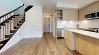 This well-appointed two-story residence offers four bedrooms and three bathrooms spread across two thoughtfully designed floors. The main level opens into a bright, open-concept kitchen and living area finished with light hardwood flooring. The kitchen is a standout feature, showcasing warm wood cabinetry that extends to the ceiling, a white quartz island, stainless steel appliances including a refrigerator, built-in microwave, dishwasher, and range, all complemented by a clean white tile backsplash. A striking staircase with a black metal railing connects the lower level to the upper floor. The upper level hosts the bedrooms, each finished with the same light hardwood flooring and featuring mirrored sliding closet doors that enhance the sense of space. The primary bedroom benefits from large windows offering urban views and access to a private balcony. The bathrooms are finished in a modern style with wood-toned floating vanities, white quartz countertops, large-format white wall tiles, and glass-enclosed showers. A dedicated laundry room with tile flooring adds convenience. Hallways on both floors connect the spaces cleanly, maintaining a cohesive, contemporary aesthetic throughout.