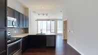This one-bedroom, one-bathroom unit offers a well-designed open-concept layout with a comfortable interior footprint complemented by an exceptionally large private outdoor terrace—nearly half the size of the interior living space—providing rare outdoor living opportunities in an urban setting.

The kitchen is a standout feature, equipped with dark espresso cabinetry extending to the ceiling, stainless steel appliances including a refrigerator, range, and built-in microwave, a mosaic tile backsplash, light quartz countertops, and a peninsula with an undermount sink that opens seamlessly to the living area. Rich, dark hardwood flooring flows consistently throughout the interior, adding warmth and continuity.

The living area is open and flexible, benefiting from floor-to-ceiling windows and a sliding glass door that connects directly to the expansive terrace. The terrace features tiled flooring, a brick parapet wall with a sleek metal railing, and panoramic views of a dense downtown skyline.

The bedroom includes a ceiling fan and access to a walk-in closet outfitted with wire shelving. The bathroom features a soaking tub with full-surround large-format beige tile and recessed lighting, delivering a clean, modern finish throughout.
