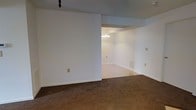 Located at 1900 Cardinal Trail Dr in Galloway, Ohio, this single-floor home offers a clean, functional layout with a straightforward and approachable design. The interior features neutral white walls throughout, providing a bright and versatile canvas that suits a variety of décor styles. Plush wall-to-wall carpeting in a warm brown tone runs through the main living areas, adding comfort underfoot and a cozy ambiance to the space. The open layout connects the living area to an adjacent room — likely a dining space — through a wide, open passageway, allowing for seamless flow between the two areas. The dining area is accented by a classic chandelier overhead, lending a touch of traditional charm to the space. White trim and baseboards line the walls, offering a clean, polished finish. Ventilation grilles are integrated neatly into the walls, and multiple electrical outlets are conveniently positioned throughout. The overall atmosphere is understated and move-in ready, with a neutral palette and classic details that provide a solid foundation for personalization and comfortable everyday living.