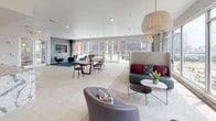 Located at 530 11th Ave N in Nashville, Tennessee, this single-floor amenity space combines contemporary design with functional, communal living. Large floor-to-ceiling windows line the lounge area, flooding the space with natural light and offering sweeping views of the Nashville skyline and surrounding cityscape. Light-toned large-format tile flooring extends throughout, creating a clean and cohesive aesthetic.

The lounge area is generously proportioned, featuring a curated mix of seating that includes a high-back sofa with accent pillows, curved armchairs, and a sleek coffee table — all anchored by a woven area rug beneath a sculptural pendant light. A dedicated dining zone accommodates a long communal table with modern side chairs, perfect for group gatherings.

The kitchen is a standout feature, outfitted with stainless steel appliances including a wall oven, gas cooktop, refrigerator with ice maker, and a built-in microwave. Rich wood cabinetry contrasts beautifully with a bold, veined marble island that seats multiple guests. A textured tile backsplash and a wall-mounted TV complete the space, making it as functional as it is visually striking. French doors provide access to an outdoor area, enhancing the open, airy atmosphere throughout.