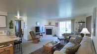 This single-floor space centers around a welcoming living room that balances comfort and functionality. The room is anchored by a tile-surround fireplace, which serves as a natural focal point and adds warmth to the overall ambiance. Neutral-toned walls and light carpet throughout contribute to a bright, airy feel. A large sliding glass door floods the space with natural light while providing a view of the outdoors, enhancing the sense of openness.

The living area is generously sized, offering ample room for a full seating arrangement that includes a plush sofa, upholstered armchair, and a classic wooden rocking chair, creating a relaxed and inviting atmosphere. A glass-top coffee table and area rug anchor the seating zone, adding definition to the space. A television and media console are thoughtfully positioned across from the seating area for comfortable viewing.

Decorative touches, including floral arrangements and wall accents, add personality without overwhelming the space. The layout flows naturally, making the room feel both practical and homey. The smooth ceiling and consistent flooring tie the space together cohesively.