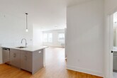 Unit 615 at 1 Main St in Bound Brook, NJ, is a thoughtfully designed one-bedroom, one-bathroom residence offering a contemporary open-concept layout. Light-toned hardwood flooring runs throughout, creating a warm and cohesive aesthetic across all living spaces. The kitchen is a standout feature, anchored by a sleek peninsula with elegant quartz countertops, a undermount sink, and pendant lighting overhead. Taupe cabinetry, a decorative hexagonal tile backsplash, and a full suite of stainless steel appliances — including a refrigerator, electric range, and microwave — complete the modern culinary space. The kitchen flows seamlessly into a combined dining and living area, which benefits from multiple windows that invite abundant natural light. The bedroom is a comfortable retreat, featuring large windows with views to the outdoors, soft gray walls, hardwood floors, and two closets for ample storage. The bathroom is finished with large-format tile, a frameless glass walk-in shower, and clean, modern fixtures. Additional conveniences include in-unit laundry and track lighting in the kitchen area, rounding out this well-appointed Bound Brook residence.