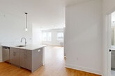 Unit 615 at 1 Main St in Bound Brook, NJ, is a thoughtfully designed one-bedroom, one-bathroom residence offering a contemporary open-concept layout. Light-toned hardwood flooring runs throughout, creating a warm and cohesive aesthetic across all living spaces. The kitchen is a standout feature, anchored by a sleek peninsula with elegant quartz countertops, a undermount sink, and pendant lighting overhead. Taupe cabinetry, a decorative hexagonal tile backsplash, and a full suite of stainless steel appliances — including a refrigerator, electric range, and microwave — complete the modern culinary space. The kitchen flows seamlessly into a combined dining and living area, which benefits from multiple windows that invite abundant natural light. The bedroom is a comfortable retreat, featuring large windows with views to the outdoors, soft gray walls, hardwood floors, and two closets for ample storage. The bathroom is finished with large-format tile, a frameless glass walk-in shower, and clean, modern fixtures. Additional conveniences include in-unit laundry and track lighting in the kitchen area, rounding out this well-appointed Bound Brook residence.