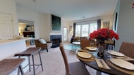 Located at 386 Attenborough Dr in Rosedale, MD, this single-floor residence offers a thoughtfully designed open-concept layout that seamlessly connects the living, dining, and kitchen areas. The living room is a standout space, anchored by a dark tile-surround fireplace with a classic white mantel and large windows that allow generous natural light to fill the room. Plush wall-to-wall carpeting runs throughout the main living areas, enhancing the warm, comfortable ambiance. A breakfast bar with barstool seating bridges the kitchen and living space, providing casual dining convenience alongside the dedicated dining area, which features soft blue-gray walls, a pendant light fixture, and space for a full round dining table. The bedroom is generously sized, offering a serene retreat with soft carpeting, large windows with curtains, and a spacious walk-in closet outfitted with wire shelving and multiple storage configurations. The full bathroom is finished with light tile flooring, warm wood cabinetry, a full-width vanity countertop, and a tub-shower combination with white subway tile surround. Overall, the space presents a cohesive, neutral palette with tasteful design details throughout.