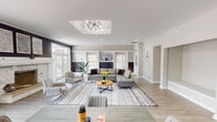 This thoughtfully designed single-floor space offers an open-concept layout that seamlessly connects the living, dining, and kitchen areas, creating a bright and welcoming atmosphere. The expansive living room serves as the centerpiece, anchored by a striking white stone fireplace with a classic wood mantel set against a bold navy shiplap accent wall. Above, a coffered ceiling detail with a Sputnik-style chandelier adds architectural character and visual interest. Large windows and French doors bathe the space in natural light, while light-toned hardwood flooring flows consistently throughout, tying the rooms together. Built-in display niches along one wall provide both functional storage and decorative opportunities. The kitchen features clean white shaker cabinetry, a light hexagonal tile backsplash, stainless steel appliances, and a double sink, all opening directly to the dining area for easy entertaining. A secondary kitchenette or utility corridor with matching white cabinetry and additional countertop space extends the functional footprint of the home. A decorative wall clock and tasteful accents contribute to the space's modern transitional aesthetic. With multiple windows offering outdoor views and a layout designed for both comfort and functionality, this space delivers a balanced blend of style and practicality.