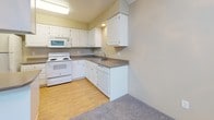This single-floor unit is organized into a practical and cohesive layout. The kitchen is well-equipped with white cabinetry, gray laminate countertops, a full-size refrigerator, electric range, built-in microwave, and dishwasher. Light wood-style flooring runs underfoot, and a peninsula provides additional counter space and separation from the adjacent living area. The living room is carpeted and features a brick fireplace, a large window, and a sliding glass door with vertical blinds that opens to a balcony overlooking mature trees, bringing in generous natural light and outdoor views. Baseboard heating units are present throughout the carpeted rooms. The bedrooms are spacious, each featuring neutral-toned carpet, baseboard heating, and windows that allow natural light in. Closet access is provided in the primary bedroom. Two bathrooms serve the unit: one includes a tub-shower combo with light wood-style flooring, while the second features a single-sink vanity with white cabinetry, a large mirror, and a separate glass-enclosed shower stall. The overall aesthetic is clean and functional, with neutral tones carried consistently throughout the space.