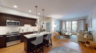 This thoughtfully designed single-floor residence offers a seamless open-concept layout that connects the kitchen, dining, and living areas into one cohesive, light-filled space. The kitchen is a standout feature, showcasing rich dark-wood cabinetry, stainless steel appliances, a subway tile backsplash, and a granite-topped island with bar seating illuminated by pendant lighting. A dedicated walk-in pantry provides generous additional storage. The kitchen flows naturally into the living room, where warm hardwood flooring, soft neutral tones, and large French doors lead to a private balcony overlooking the surrounding neighborhood. Two well-proportioned bedrooms offer comfortable retreats; the primary bedroom features a ceiling fan, warm accent wall, and access to an en-suite bathroom with a walk-in shower, penny tile flooring, and a white vanity. The second bedroom is bright and airy, benefiting from natural light through a large window. A second full bathroom includes a tub-shower combination and matching penny tile flooring. Throughout the residence, consistent hardwood flooring, recessed lighting, and a clean, neutral color palette create a cohesive and inviting atmosphere suited for everyday living.
