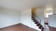 This well-appointed three-floor residence offers a thoughtfully designed layout spread across multiple levels, providing distinct areas for living, relaxation, and everyday function. The interior is characterized by a clean, contemporary aesthetic, with crisp white walls and smooth ceilings that create a bright and airy atmosphere throughout.

Warm-toned hardwood flooring runs through the main living area, adding a sense of warmth and continuity to the space. A standout architectural feature is the staircase connecting the floors, which combines rich dark wood treads with sleek black metal railings — a modern detail that serves as both a functional element and a visual focal point.

The open layout of the main level provides a versatile living area that feels spacious and uncluttered, allowing for flexible furniture arrangements to suit a variety of lifestyles. The neutral color palette throughout enhances the sense of light and space, making each floor feel welcoming and easy to personalize.

With three full floors, this residence offers generous vertical living space, ensuring clear separation between living, sleeping, and utility areas. The overall ambiance is modern and understated, with quality finishes that reflect a commitment to both style and practicality.