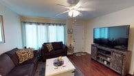 This single-story residence offers a well-organized layout with distinct living, dining, sleeping, and bathing spaces, each thoughtfully finished to create a comfortable and functional environment.

The living room serves as the heart of the home, featuring rich hardwood flooring, a textured ceiling, and a ceiling fan with integrated lighting. Large windows dressed with sheer grommet curtains allow natural light to fill the room, while a wall-mounted flat-screen television and a rustic whitewashed coffee table add character. Dark upholstered sofas provide ample seating, complemented by a distressed wood media console.

The dining area transitions naturally from the living space, showcasing the same hardwood flooring. A round dark-wood table with matching cross-back chairs sits beneath a pendant light, creating an intimate setting for meals.

Two bedrooms feature plush carpeting, ceiling fans, and windows with curtain panels. The primary bedroom includes a whitewashed wood bed frame and matching dresser, while the second bedroom showcases an upholstered headboard and a curated gallery wall arrangement.

Two bathrooms mirror each other in layout, each equipped with a single vanity, built-in mirror, overhead lighting, and a shower-tub combination.