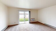 Located at 1610 Schaefer Cir in Appleton, Wisconsin, this single-floor, 2-bedroom, 1-bathroom unit offers a practical and comfortable layout. The living area is carpeted and generously sized, featuring a wall-mounted air conditioning unit and baseboard heating — ideal for Wisconsin's varied climate. Natural light enters through the front entry door, and the space transitions smoothly into the kitchen area, which is visible from the living room and features tile flooring, white cabinetry, and appliances including a stovetop range. The spacious primary bedroom is notably large, complete with carpeting, baseboard heating, and a closet with louvered doors. The second bedroom is bright and cozy, benefiting from a window with a view of the surrounding neighborhood and its own baseboard heater. Both bedrooms feature light wood door trim that complements the neutral, cream-toned walls throughout. The full bathroom is well-appointed with large-format tile flooring, a tub-shower combination surrounded by green ceramic wall tile, a wooden vanity with a white countertop, and a large mirror. The overall aesthetic is clean, neutral, and functional — well-suited for comfortable everyday living.