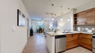 This 650 square foot one-bedroom apartment offers a harmonious blend of style and functionality. The open-concept layout maximizes space, seamlessly connecting the living room and kitchen. The living area features light wood flooring, a comfortable gray sofa, and modern artwork, creating an inviting atmosphere.

The kitchen boasts warm wood cabinetry, stainless steel appliances, and granite countertops. A breakfast bar with stylish stools provides additional seating and dining space. Pendant lighting adds a touch of elegance to the culinary area.

The bedroom, spanning 150 square feet, is a serene retreat with plush carpeting, a queen-sized bed, and soothing teal accents. A large window allows natural light to flood the space, while a ceiling fan ensures comfort. A substantial dresser and closet offer ample storage.

The bathroom features neutral-toned tile flooring and a shower/tub combination. Throughout the apartment, crisp white walls provide a clean backdrop for the contemporary furnishings and decor. The overall design aesthetic is modern and cohesive, making efficient use of the compact space while maintaining a sense of openness and style.