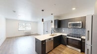 Located at 8327 Ridge Ave in Philadelphia's Roxborough neighborhood, this thoughtfully designed one-bedroom, one-bathroom unit offers a clean, modern aesthetic across a single floor. The open-concept kitchen and living area serves as the heart of the home, featuring dark cabinetry with gold hardware, a light quartz peninsula with an undermount sink, blue-gray subway tile backsplash, and a full suite of stainless steel appliances including a refrigerator, range, microwave, and dishwasher. Pendant lighting over the peninsula adds a contemporary touch, while warm wood-look flooring flows throughout the space. The living area is bright and airy, benefiting from natural light through a window overlooking greenery outside. The bedroom is a comfortable, well-proportioned retreat with warm hardwood-style flooring, a window with outdoor views, a wall-mounted HVAC unit, and direct access to a dedicated closet with built-in shelving. The bathroom is finished with large-format light gray floor tiles, a dark vanity with gold accents, a mirrored medicine cabinet, and a full bathtub with shower. Clean white walls and recessed lighting throughout give the entire unit a fresh, move-in-ready feel.