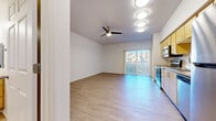This single-floor unit is designed with a clean, contemporary aesthetic and a practical open layout. Light wood-tone flooring runs consistently throughout the space, creating a cohesive and airy feel. The living area is bright and open, benefiting from natural light that streams in through a sliding glass door fitted with vertical blinds, which leads to a balcony with views of the surrounding neighborhood. A ceiling fan overhead adds both functionality and a finishing touch to the living space.

The kitchen is well-appointed and positioned along one wall, featuring light wood cabinetry with ample upper and lower storage, granite-look countertops, a tiled backsplash, and a full suite of stainless steel appliances including an electric range, over-the-range microwave, dishwasher, and refrigerator. The layout allows for an efficient workflow while remaining visually open to the rest of the unit.

The bedroom is a comfortable, well-proportioned space with its own ceiling fan and easy access to the bathroom. The bathroom includes a combination tub and shower, a warm wood-toned vanity with storage drawers, and bright overhead lighting above the mirror. An adjacent walk-in closet provides generous built-in shelving and hanging space.