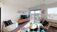This thoughtfully designed single-floor unit offers a seamless open-concept layout that integrates the kitchen, living, and sleeping areas into one cohesive, light-filled space. Warm hardwood-style flooring flows throughout, complementing the clean white walls and contemporary finishes.

The kitchen is well-appointed with white cabinetry, light quartz countertops, a bold dark tile backsplash, and a full suite of stainless steel appliances, including a refrigerator, electric range, built-in microwave, and dishwasher. A single-basin undermount sink with a modern arc faucet completes the functional workspace.

The open living area is bathed in natural light from large windows and a sliding glass door that leads directly to a private balcony, offering elevated views of the surrounding neighborhood. The sleeping area is defined within the open floor plan, providing a comfortable and flexible arrangement.

The bathroom includes a full tub-shower combination and connects to a dedicated closet space with built-in shelving, as well as an in-unit stacked washer and dryer — a practical and convenient feature. The overall ambiance is clean and contemporary, with an airy feel enhanced by abundant natural light throughout.