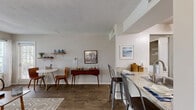 This thoughtfully designed one-bedroom, one-bathroom residence in Columbia, Maryland offers a functional and comfortable single-floor layout. The living room serves as the heart of the home, featuring wood-style flooring, neutral toned walls, and a classic fireplace framed by two windows that invite natural light and outdoor views — creating a warm, inviting atmosphere. The open layout connects the living area to the kitchen and dining space, which is equipped with light wood cabinetry, black appliances including a refrigerator and electric range, granite-style countertops, and a breakfast bar with seating. The dining area flows naturally from the kitchen, providing a versatile space for everyday meals or entertaining. The bedroom is a serene retreat with plush carpet flooring, a textured ceiling, and a sliding glass door offering direct access to a private outdoor area and greenery views. The full bathroom features warm earth-toned tile surround on the tub/shower combination, wood-style flooring, and a vanity with ample mirror space. A dedicated closet and hallway round out the layout, providing practical storage solutions. The residence combines functional design with comfortable finishes throughout.