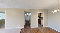 Located at 1246 Mooty Bridge Rd in LaGrange, Georgia, this single-story, 3-bedroom, 2-bathroom home offers a well-organized and comfortable layout. Rich, dark hardwood-style flooring runs through the main living areas, complemented by warm neutral beige walls and textured ceilings throughout. The living room flows naturally into a hallway that connects the key areas of the home. The dining room is highlighted by an elegant chandelier and the same warm hardwood flooring, creating an inviting atmosphere for meals and gatherings. The kitchen is efficiently designed with rich wooden cabinetry, granite-style countertops, a stainless steel sink, and white appliances, providing both functionality and style. Each of the three bedrooms features plush carpeting and natural light from windows with outdoor views of surrounding greenery. The spacious primary bedroom includes a generous closet with built-in shelving. The secondary bedrooms are well-proportioned and equally comfortable. Both bathrooms are finished with warm wood vanities, white countertops, and full tub-shower combinations with clean white tile surrounds. Two hallways connect the rooms seamlessly, with two closets offering practical storage solutions throughout this inviting home.