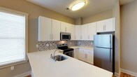 This 1-bedroom, 1-bathroom residence is thoughtfully designed to offer both functionality and modern style across a single floor. The kitchen serves as a standout feature, showcasing crisp white shaker-style cabinetry that extends to the upper walls, providing generous storage space. Stainless steel appliances — including a refrigerator, electric range, and built-in microwave — lend a sleek, contemporary feel to the space. A mosaic tile backsplash in neutral earth tones adds a touch of texture and visual interest, complementing the clean white countertops that wrap around the kitchen and extend to a peninsula with an integrated sink. The flush-mount ceiling light provides bright, even illumination throughout the kitchen area. The overall design aesthetic is clean and modern, with a neutral color palette of warm beige walls and white cabinetry that creates a cohesive and inviting atmosphere. The open layout of the kitchen allows for easy movement and accessibility, making it a practical and welcoming space for everyday living. The single-floor layout ensures convenient, step-free living throughout the entire residence.