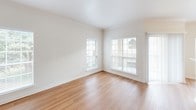 This well-appointed single-floor residence offers a clean, modern aesthetic defined by neutral tones, crisp white walls, and an abundance of natural light. The open-concept layout seamlessly connects the kitchen and living areas, creating a welcoming and functional flow throughout the space. The kitchen features white cabinetry, stainless steel appliances including a range and built-in microwave, a breakfast bar peninsula, and pendant lighting overhead — making it both practical and visually appealing. The adjacent dining and living areas are bathed in natural light through large windows dressed with horizontal blinds, and warm hardwood-style flooring extends throughout these common spaces. Crown molding adds a refined architectural touch to the living areas. The bedroom is generously sized, featuring soft wall-to-wall carpeting, a ceiling fan with integrated light fixture, and a window that invites natural light. A walk-in closet with built-in shelving provides ample storage. The bathroom is well-equipped with a white vanity offering countertop space and storage, a tall linen cabinet, and hardwood-style flooring that ties the space together. The unit's overall design prioritizes light, openness, and a move-in-ready simplicity that suits a variety of lifestyles.