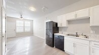 This 550 square foot apartment in Bettendorf, Iowa offers a thoughtful layout that maximizes space and functionality. The single-floor plan comprises one bedroom, measuring 130 square feet, a full bathroom, a kitchen, and a dedicated laundry area. The kitchen is a standout feature, boasting sleek white cabinetry, contrasting black appliances including a large refrigerator, stove, and built-in microwave. Light wood-look flooring throughout the main living areas creates a sense of warmth and continuity. The bedroom features plush carpeting and large windows with blinds, allowing for ample natural light. The bathroom is spacious and modern, with a tub-shower combination, white fixtures, and wood-look flooring that mirrors the main living area. In-unit laundry adds convenience to this compact living space. The neutral color palette throughout provides a blank canvas for personalization, while the modern finishes give the apartment a fresh, contemporary feel. This efficient layout is ideal for those seeking a low-maintenance lifestyle without sacrificing style or amenities.