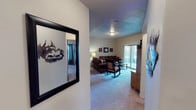 This single-floor residence offers a cohesive rustic aesthetic throughout its well-organized layout. The living room serves as the central gathering space, featuring plush carpet, a sliding glass door that opens to an outdoor patio, and ample room for seating and entertainment. Natural light filters in through the large sliding door, providing views of the exterior surroundings. Decorative touches, including wildlife-themed metal wall art and a wagon wheel accent, reinforce the space's rustic character.

The kitchen is outfitted with warm knotty wood cabinetry, dark countertops, tile flooring, and black appliances including a range and built-in microwave. A separate dining area features tile flooring and a round wooden dining table, accented by a circular wall mirror.

The primary bedroom offers carpet, a large window with outdoor views, and direct access to an adjoining room. Additional bedrooms are similarly carpeted, with one featuring a walk-in closet. The bathroom includes tile flooring, a vanity with wood cabinetry, and a full tub-shower combination. Throughout the home, textured ceilings and neutral wall tones provide a clean, consistent backdrop.