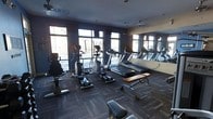 This fitness center is designed to offer a comprehensive workout environment within a single-floor layout. The space is furnished with a variety of cardio equipment, including treadmills, elliptical trainers, and stationary bikes, providing ample options for aerobic exercise. A large mirror spans one wall, creating a sense of depth and allowing users to monitor their form during workouts. The room is brightened by a row of large windows along the exterior wall, inviting natural light and offering views of the surrounding outdoor environment. The ceiling features recessed lighting and ventilation fixtures, ensuring the space remains well-lit and properly ventilated. Durable, patterned carpet tiles cover the floor, providing both comfort and practicality underfoot. A weight bench with free weights rounds out the equipment selection, supporting strength training alongside cardio workouts. The walls are painted in a cool, neutral tone that contributes to a focused and energizing atmosphere. The overall design is functional and modern, catering to a range of fitness needs in a clean, organized setting.